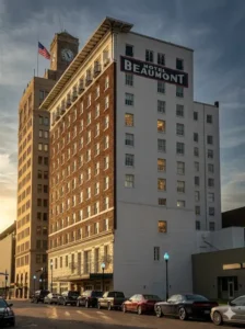 View of the historic Hotel Beaumont building in downtown Towing Service in Beaumont TX showing its brick facade, signage, and several parked cars along the street during sunset.
